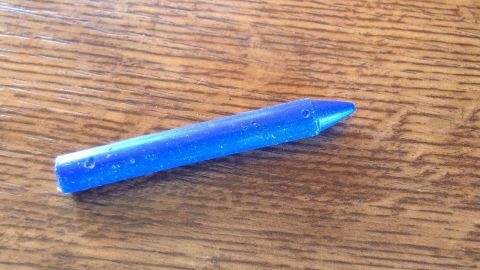 Mit Babyfeuchttüchern kann man sehr gut Flecken von Wachsmalkreide vom Holzschrank entfernen. Ein blauer Wachsmalstift liegt auf einem Holztisch, bereit, Flecken zu verursachen, die mit Babyfeuchttüchern entfernt werden müssen.