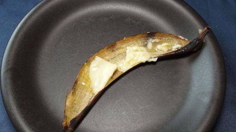 Eine mit Butter bestrichene Bananenschale als Rosendünger. Eine Banane mit Butter liegt auf einem schwarzen Teller und zeigt eine Mischung aus gelb-brauner Farbe.