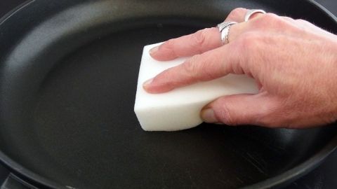 Eine beschichtete Pfanne mit Schmutzradierer reinigen. Eine Hand reinigt eine beschichtete Pfanne mit einem Schmutzradierer, um Ablagerungen zu entfernen.