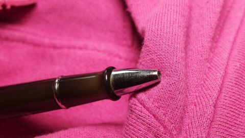 Kugelschreiberflecken auf der Kleidung mit klarem Schnaps, z. B. Wodka, vorbehandeln und dann normal waschen. Ein Kugelschreiber liegt auf einem pinken Kleidungsstück, bereit, einen Fleck zu hinterlassen.