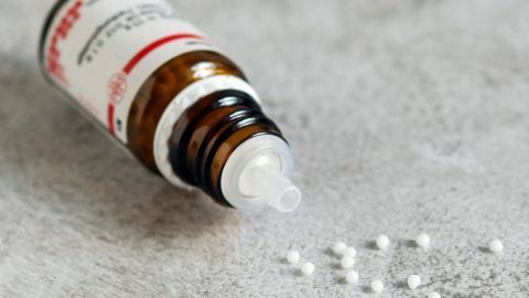 Das homöopathische Mittel Sabadilla D 12 hilft bei Kopfläusen - sowohl vorbeugend als auch bei akutem Befall. Eine Flasche Homöopathie steht auf einer Oberfläche, während weiße Kügelchen daneben verstreut liegen.