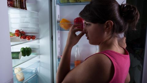Gestört von unangenehmen Gerüchen im Kühlschrank? Diese Methode zeigt dir, wie du die frischen Aromen von Kaffee nutzen kannst, um unangenehme Gerüche effektiv zu neutralisieren. Perfekt für ein angenehmes Kühlschrankklima. Eine Frau steht vor einem offenen Kühlschrank, hält sich die Nase zu und zeigt Unbehagen durch einen unangenehmen Geruch.