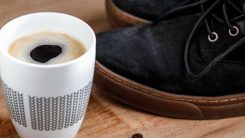 Wenn sich auf deinen Schuhen Salz- und Schneeränder befinden, bekommst du sie weg, indem du sie mit kaltem Kaffee einreibst. Schwarze Schuhe stehen neben einer Tasse Kaffee und Kaffeebohnen auf einer Holzoberfläche, um Salzränder zu entfernen.