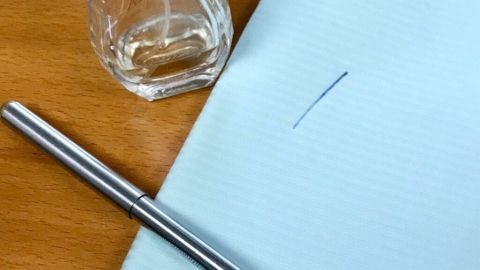 Mithilfe von Kölnisch Wasser (4711) können Kugelschreiberflecken aus Wäsche erfolgreich entfernt werden. Ein silberner Kugelschreiber liegt auf einem blauen Papier neben einer Flasche 4711, die für Fleckenentfernung genutzt wird.