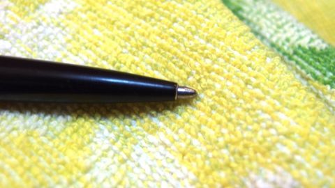 Mithilfe von 4711 Duftwasser lassen sich Kugelschreiberflecken entfernen. Ein schwarzer Kugelschreiber liegt auf einem gelben Tuch, bereit, Flecken zu hinterlassen.