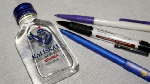 Einfach den Wodka auf den Fleck tröpfeln und etwas einziehen lassen danach mit einem sauberen, feuchten Tuch abtupfen.. Eine Wodkaflasche liegt neben mehreren Kugelschreibern auf einer Oberfläche, bereit, um Flecken zu entfernen.