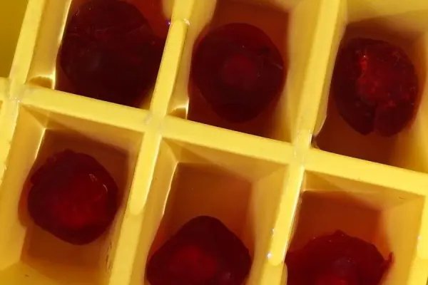 Kugelförmige, rote Eiswürfel liegen in einem gelben Eiswürfelformer in einer kühlen Umgebung, bereit zum Servieren.