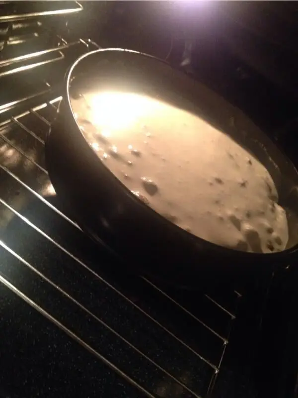 Der Stachelbeerkuchen backt im Ofen und entwickelt eine goldene Baiserhaube, umgeben von dunkler Ofenhitze.