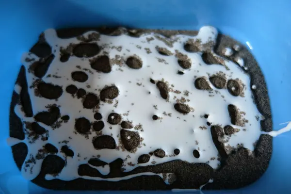 Eine Sandschale wird in einer blauen Schüssel aus feuchtem Sand und weißem Kleber geformt, während die Materialien miteinander vermischt werden.