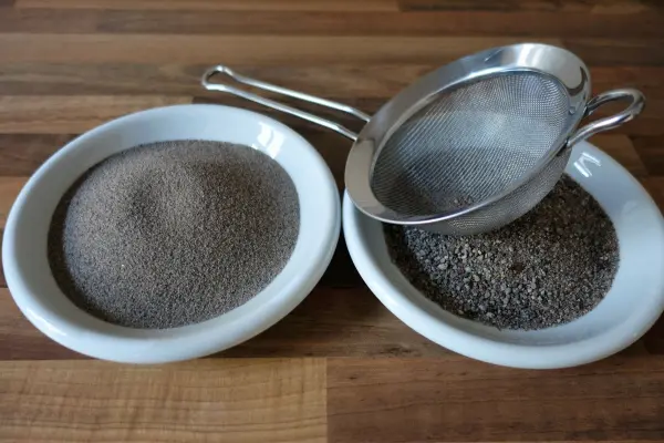 Auf einer Holzoberfläche stehen zwei Schalen mit Sand, während ein Sieb den Sand siftet, ideal für eine Sandschale.