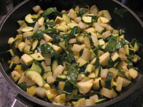In einer Pfanne werden frisch zubereitete Gemüseblätter und Stücke von Zucchini und anderem Gemüse sautiert.