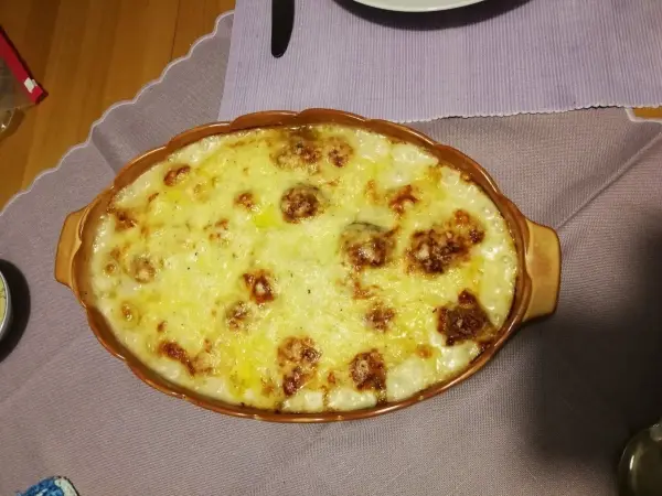Ein Auflauf aus Rosenkohl und Hackbällchen wird goldbraun überbacken auf einem Tisch serviert, umgeben von Geschirr.