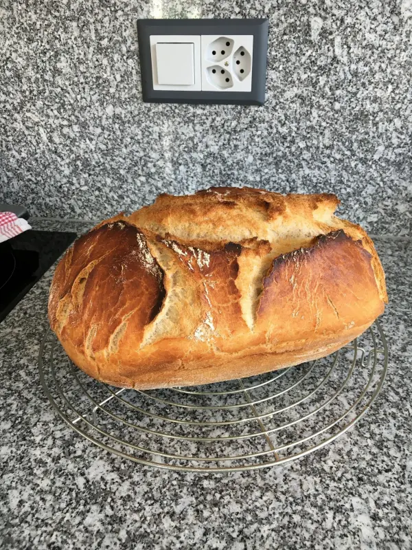 Ein frisch gebackenes Dinkel-Roggenbrot liegt auf einem Kuchengitter in einer modernen Küche, umgeben von grauem Granit.