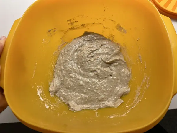 Eine gelbe Schüssel enthält einen glatten, dicken Sauerteig, der zum Backen von Roggenmischbrot vorbereitet wird.