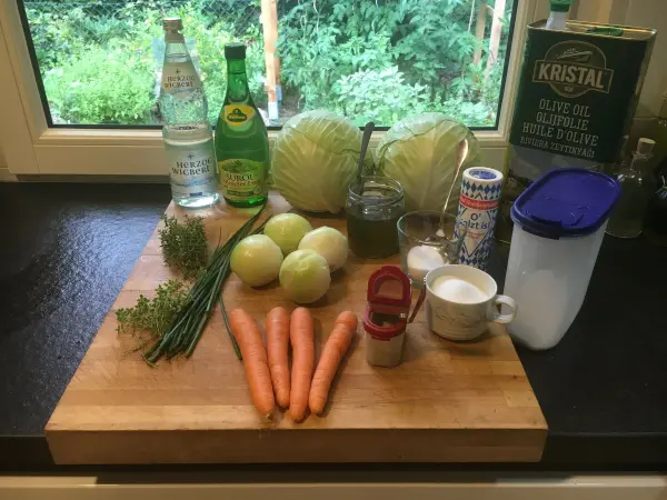 Auf einem Holzbrett liegen frische Zutaten wie Weißkohl, Karotten und Äpfel, bereit zur Zubereitung von Krautsalat.