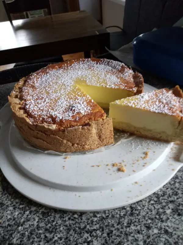 Ein Käsekuchen liegt auf einem weißen Teller, ein Stück wurde herausgeschnitten, um ihn zu probieren.