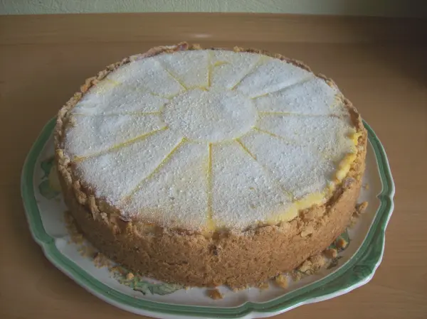 Ein Käsekuchen mit einer leichten Zuckerglasur, präsentiert auf einem eleganten Teller, steht auf einer Holzoberfläche.