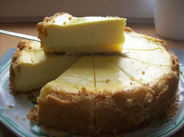 Ein Käsekuchen wird auf einem Teller serviert, aus dem ein Stück herausgeschnitten wurde und der Kuchen einen goldgelben Farbton hat.