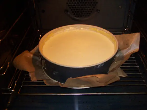 Ein Käsekuchen backt im Ofen, umgeben von Backpapier, während die Hitze gleichmäßig auf die Mischung einwirkt.