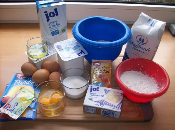 Auf einem Tisch liegen verschiedene Zutaten für einen perfekten Käsekuchen: Eier, Quark, Zucker und Butter in Schüsseln.
