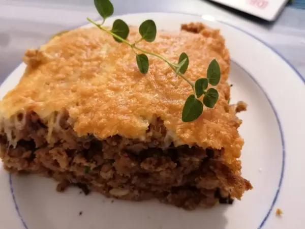 Ein Stück Lasagne liegt auf einem Teller, dampfend und goldbraun gebacken, garniert mit frischen Kräutern.