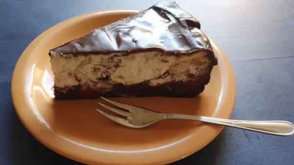 Ein Stück Schwarzwälder Käsekuchen liegt auf einem braunen Teller, bereit zum Genießen, mit einer Gabel daneben.
