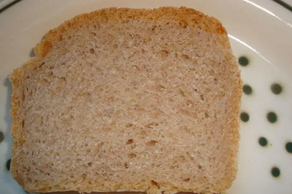 Ein Stück Dinkelbrot liegt auf einem Teller mit grünen Punkten, frisch geschnitten und bereit zum Verzehr.