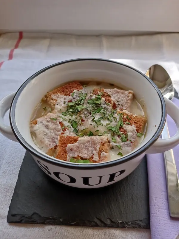 Eine dampfende Schüssel französischer Zwiebelsuppe mit Käse und Croutons, serviert auf einem schwarzen Steinbrett.