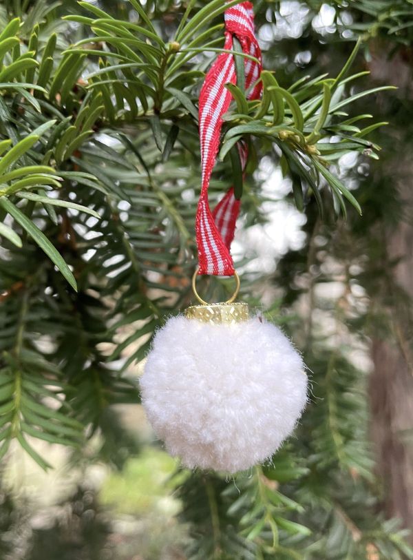 Wei&szlig;e Weihnachtskugel aus selbstgemachtem Pompom an einem Tannenzweig.