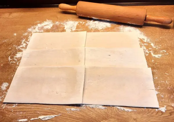 Die Arbeitsfläche wird leicht mit Mehl bestreut und die Teigplatten werden überlappend ausgewellt.