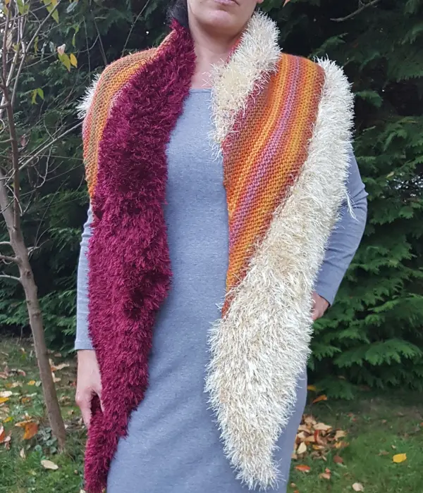 Sämtliche Wollreste können hier verarbeitet werden, wenn sie ähnliche Wascheigenschaften haben. Eine Person trägt eine gestrickte, bunte, herbstliche Stola mit flauschigen Rändern in einem grünen Garten.