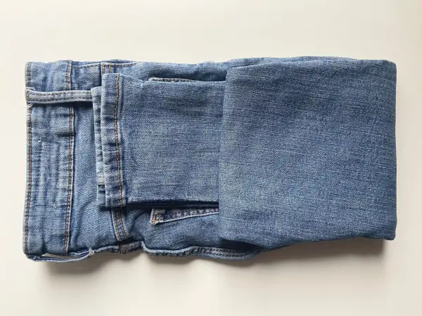 Falte deine Jeans einmal zur Mitte hoch und im Anschluss ein zweites Mal, um ein kleines P&auml;ckchen zu erhalten.