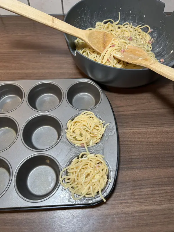 Verteile die Spaghettimischung jetzt auf die zw&ouml;lf Muffinf&ouml;rmchen. Nimm dabei nur wenige Nudeln zwischen das Salatbesteck, sonst werden die F&ouml;rmchen zu voll. Au&szlig;erdem kleckerst du so auch weniger.