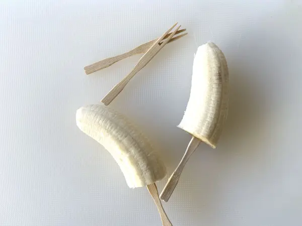 Nun steckst du Holzspieße in die Bananenhälften. Wenn du magst, kannst du sie auch für einen kurzen Kälteausflug in dein Gefrierfach stecken. So halten sie auch gleich besser. Nun steckst du Holzspieße in die Bananenhälften. Wenn du magst, kannst du sie auch für einen kurzen Kälteausflug in dein Gefrierfach stecken. So halten sie auch gleich besser.