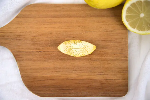 Schneide die Zitronenschale ovalförmig aus und mache mittig einen kleinen Schnitt. Schneide die Zitronenschale ovalförmig aus und mache mittig einen kleinen Schnitt.