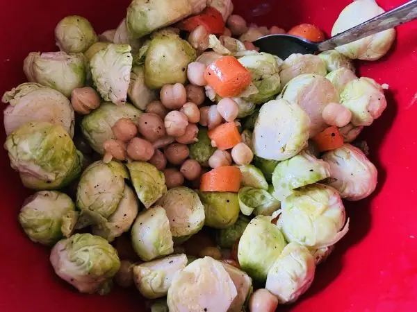 Rosenkohl, Kichererbsen und Möhren werden mit Öl, Salz und Pfeffer in einer Schüssel angerührt. Rosenkohl, Kichererbsen und Möhren werden mit Öl, Salz und Pfeffer in einer Schüssel angerührt.