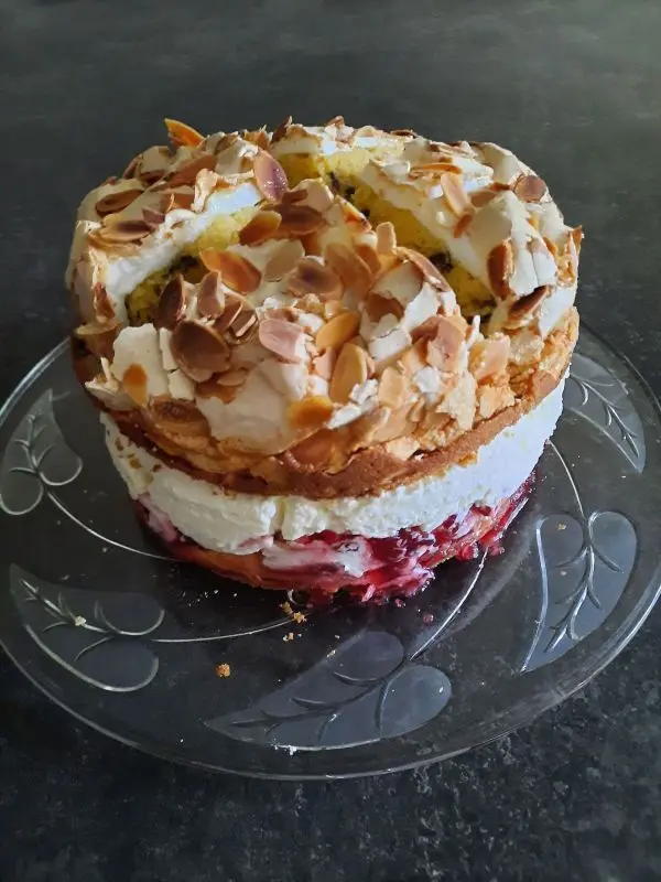 Fertig ist eine verführerische Baisertorte mit Preiselbeersahnefüllung und Mandelplättchen. Preiselbeer-Baiser-Torte mit Sahneschicht und knusprigen Mandelblättchen auf Glasplatte gegen dunklen Hintergrund.