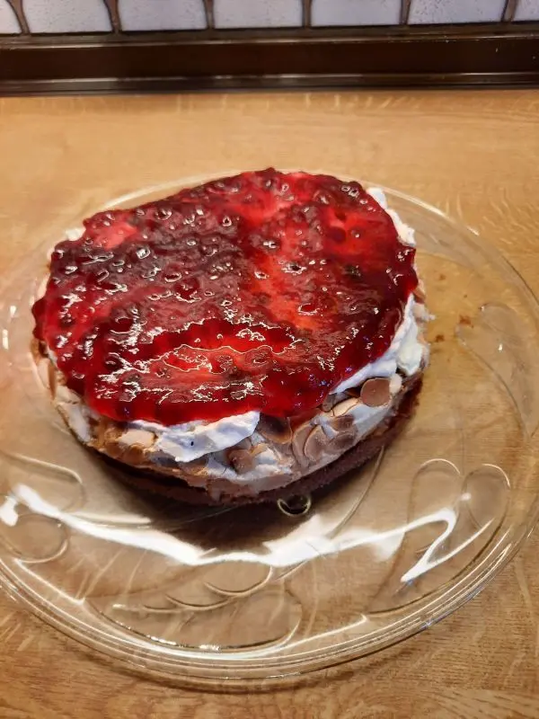 Die Preiselbeeren wurden auf dem Sahnebelag gleichmäßig verteilt. Sie verleihen der Torte eine farbige Optik. Preiselbeer-Baiser-Torte mit knusprigen Mandeln und Sahneschicht auf Glasplatte auf einem Holztisch