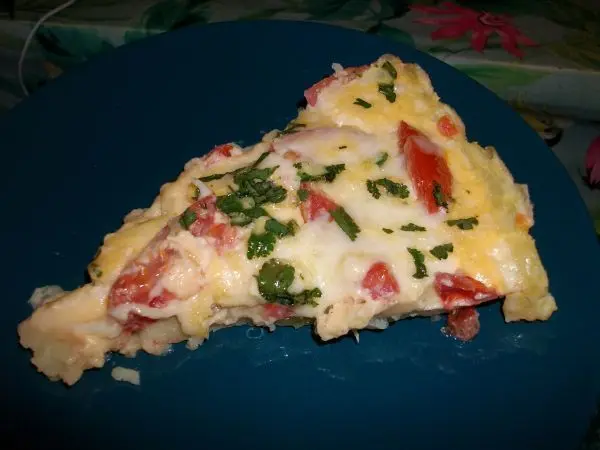 Kartoffelpizza ohne Mehl mit Tomaten, K&auml;se und frischen Kr&auml;utern auf einem blauen Teller