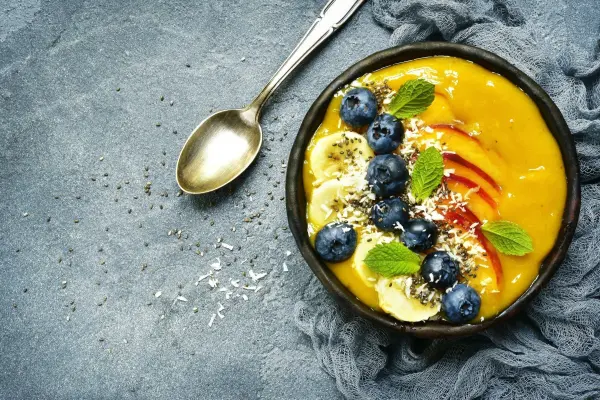 Die Basis der tropische Smoothie Bowl besteht aus Mango, gefrorener Banane, Pfirsich. Dazu passen Kokosflocken und Bananenchips.