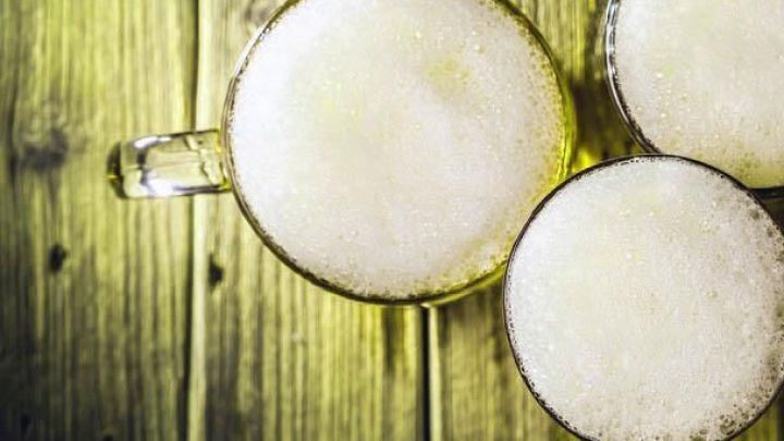 Schaumige Butterbier in Gl&auml;sern steht auf einem rustikalen Holztisch, bereit zum Genie&szlig;en in einem gem&uuml;tlichen Ambiente.