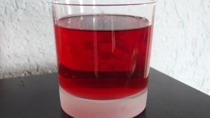 Ein Glas Kirschsaft steht auf einem Tisch. Der Saft hat eine kr&auml;ftige rote Farbe und reflektiert das Licht.