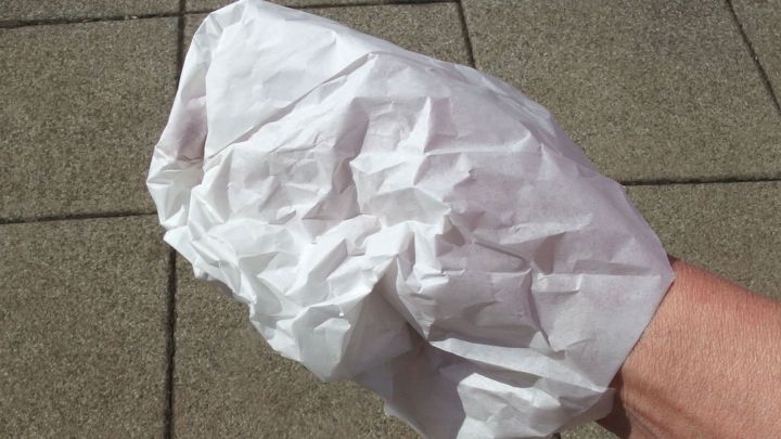 Eine Hand h&auml;lt einen zerkn&uuml;llten wei&szlig;en Handschuh, der auf einem belebten Gehweg in der Sonne liegt.