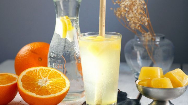 Ein frischer Drink aus echter Fruchtler und Eisw&uuml;rfeln wird in einem Glas serviert, umgeben von Orangen und elegantem Zubeh&ouml;r.