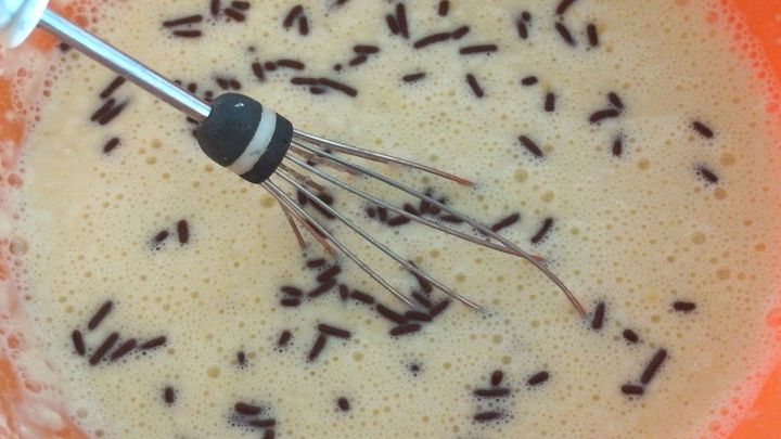 Ein R&uuml;hrbesen vermischt einen Teig mit Schokoladenst&uuml;ckchen in einer orangen Sch&uuml;ssel, bereit f&uuml;r leckere Pfannkuchen.