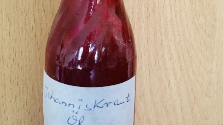 Eine kleine Flasche mit Johanniskraut&ouml;l steht auf einem Holzuntergrund, bereit zur Behandlung von Hautreizungen.