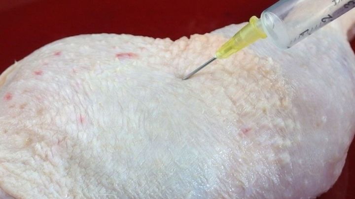 Eine Spritze injiziert Gew&uuml;rze in ein St&uuml;ck rohes Gefl&uuml;gel, um den Geschmack im K&uuml;chenumfeld zu intensivieren.