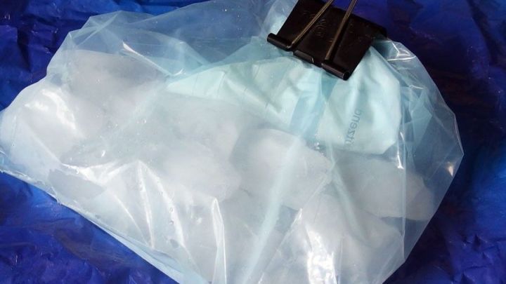 Eine Plastikt&uuml;te gef&uuml;llt mit Eisw&uuml;rfeln ist mit einer Klammer verschlossen und liegt auf einer blauen Unterlage.