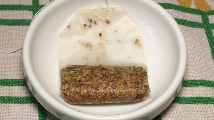 Ein gebrauchter Teebeutel liegt in einer wei&szlig;en Sch&uuml;ssel, aufgeweicht und umgeben von einem karierten Tuch im Hintergrund.