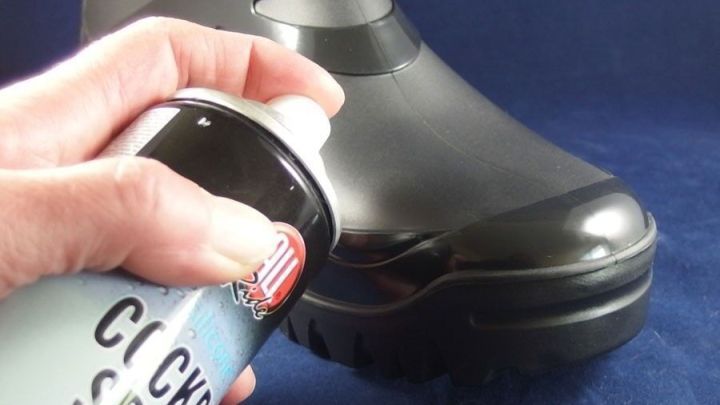 Ein schwarzer Gummistiefel wird mit Cockpitspray poliert, w&auml;hrend eine Hand die Spraydose h&auml;lt. Der Hintergrund ist dunkel.